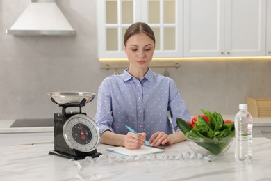 Photo of Woman developing diet plan at white marble table indoors