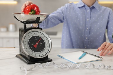 Photo of Woman weighting bell pepper on kitchen scale at white marble table indoors, closeup