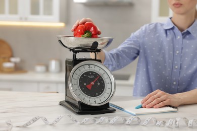 Photo of Woman weighting bell pepper on kitchen scale at white marble table indoors, closeup
