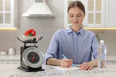 Photo of Woman developing diet plan at white marble table indoors