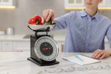Photo of Woman weighting vegetables on kitchen scale at white marble table indoors, closeup