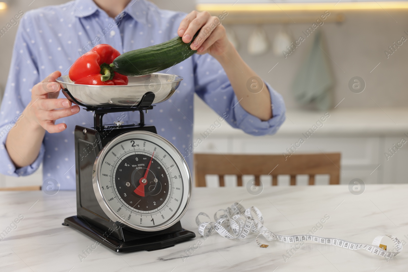 Woman weighting vegetables on kitchen scale at white marble table indoors, closeup. Space for text Photo of Woman weighting vegetables on kitchen scale at white marble table indoors, closeup. Space for text