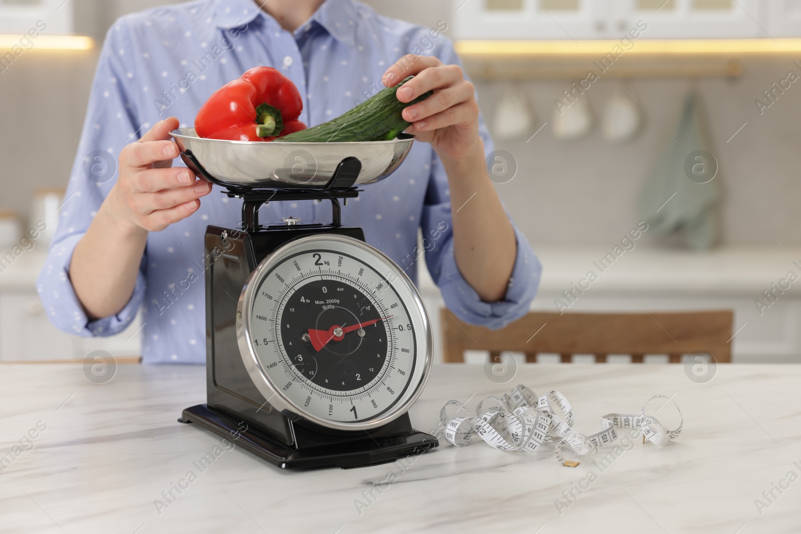 Woman weighting vegetables on kitchen scale at white marble table indoors, closeup. Space for text Photo of Woman weighting vegetables on kitchen scale at white marble table indoors, closeup. Space for text