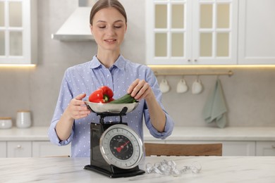 Photo of Woman weighting vegetables on kitchen scale at white marble table indoors, space for text