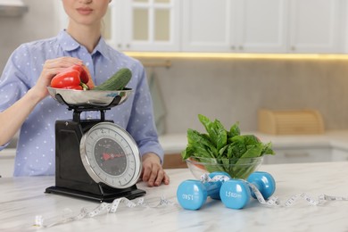 Photo of Woman weighting vegetables on kitchen scale at white marble table indoors, closeup