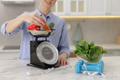 Photo of Woman weighting vegetables on kitchen scale at white marble table indoors, closeup