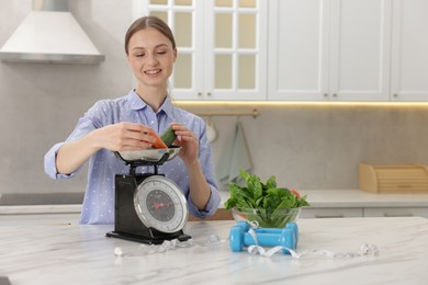 Photo of Woman weighting vegetables on kitchen scale at white marble table indoors, space for text