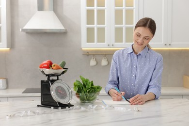 Photo of Woman developing diet plan at white marble table indoors