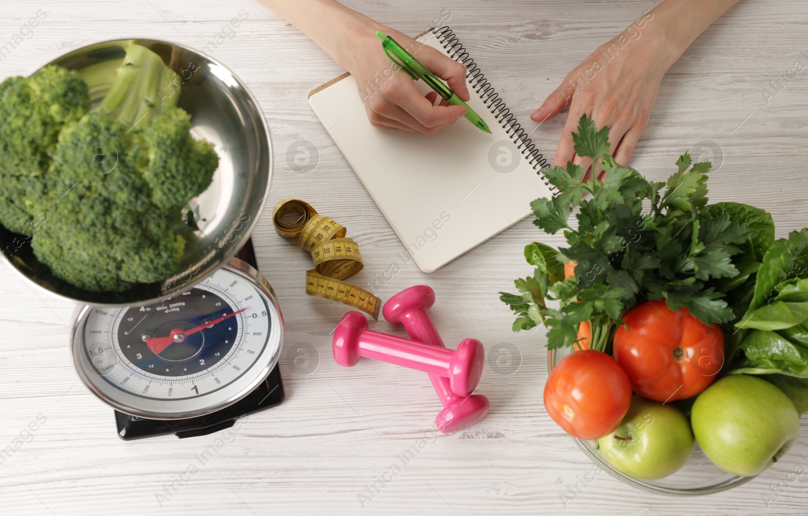 Woman developing diet plan at light wooden table with healthy food, kitchen scale, measuring tape and dumbbells, top view Photo of Woman developing diet plan at light wooden table with healthy food, kitchen scale, measuring tape and dumbbells, top view
