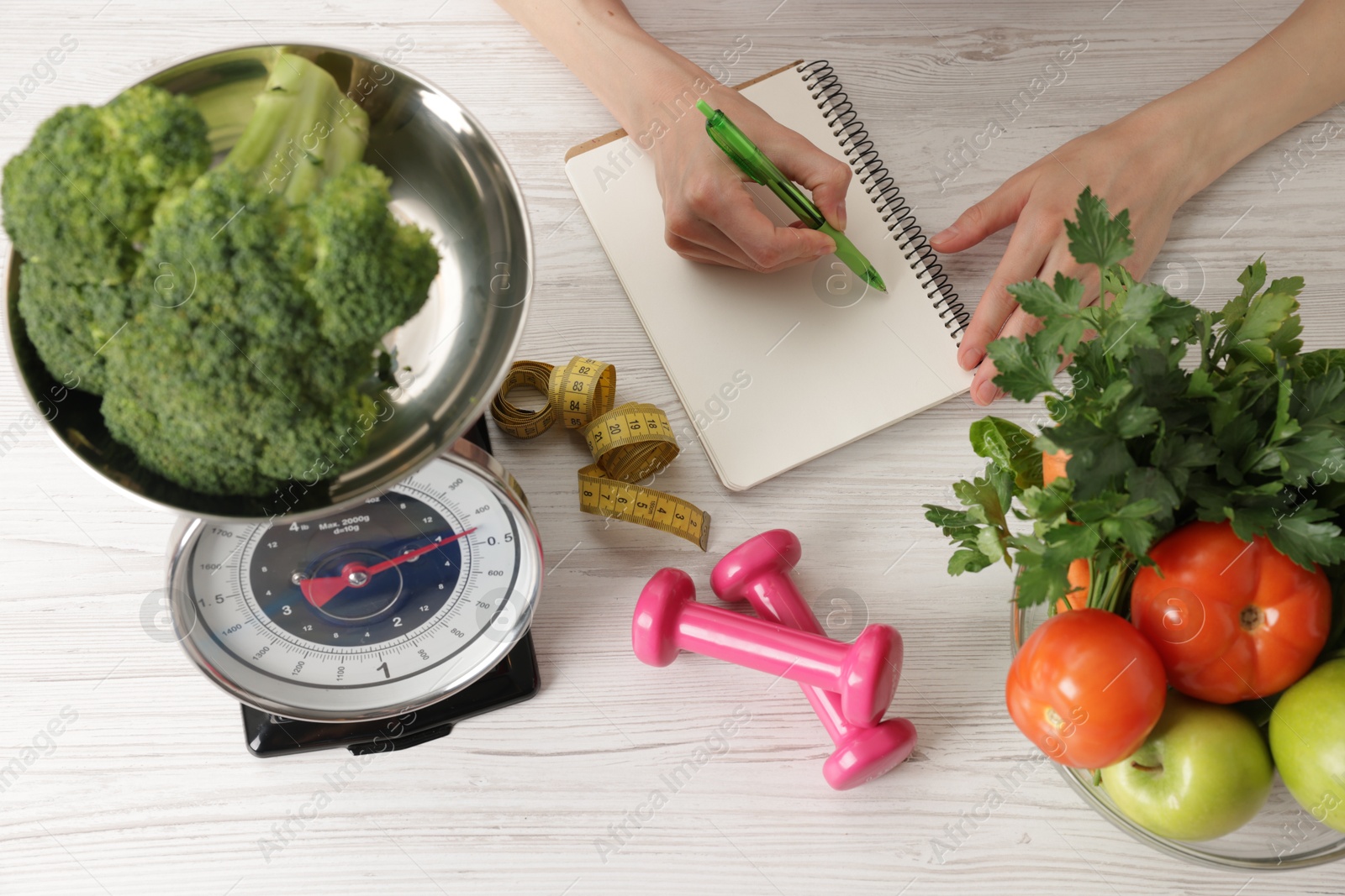 Woman developing diet plan at light wooden table with healthy food, kitchen scale, measuring tape and dumbbells, top view Photo of Woman developing diet plan at light wooden table with healthy food, kitchen scale, measuring tape and dumbbells, top view