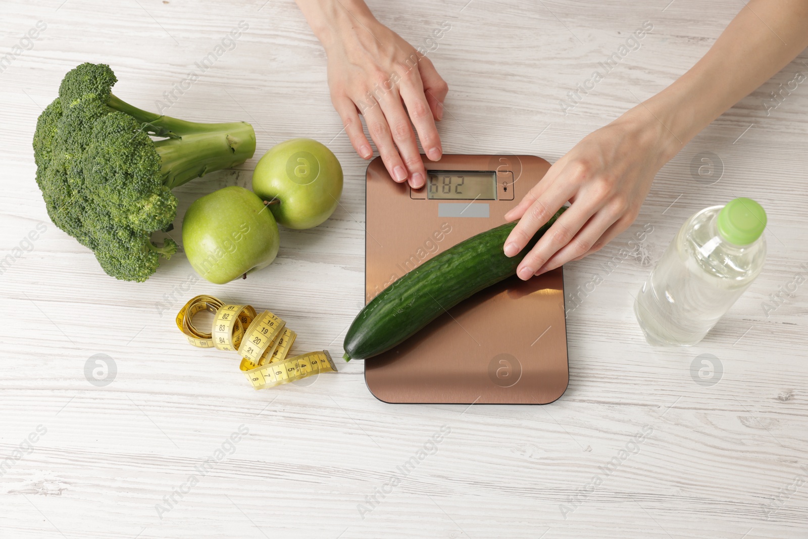 Woman with smartphone weighting cucumber on kitchen scale at light wooden table, top view Photo of Woman with smartphone weighting cucumber on kitchen scale at light wooden table, top view