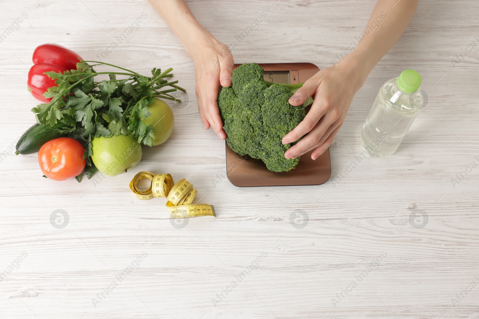 Woman weighting broccoli on kitchen scale at light wooden table, top view Photo of Woman weighting broccoli on kitchen scale at light wooden table, top view