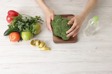 Photo of Woman weighting broccoli on kitchen scale at light wooden table, top view