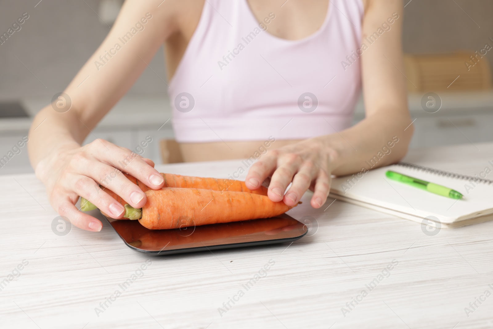 Woman weighting carrots on kitchen scale at white wooden table indoors, closeup Photo of Woman weighting carrots on kitchen scale at white wooden table indoors, closeup