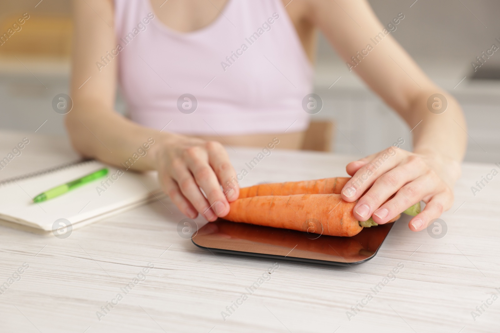Woman weighting carrots on kitchen scale at white wooden table indoors, closeup Photo of Woman weighting carrots on kitchen scale at white wooden table indoors, closeup
