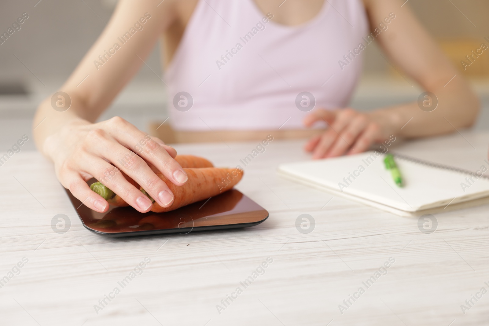 Woman weighting carrots on kitchen scale at white wooden table indoors, closeup Photo of Woman weighting carrots on kitchen scale at white wooden table indoors, closeup