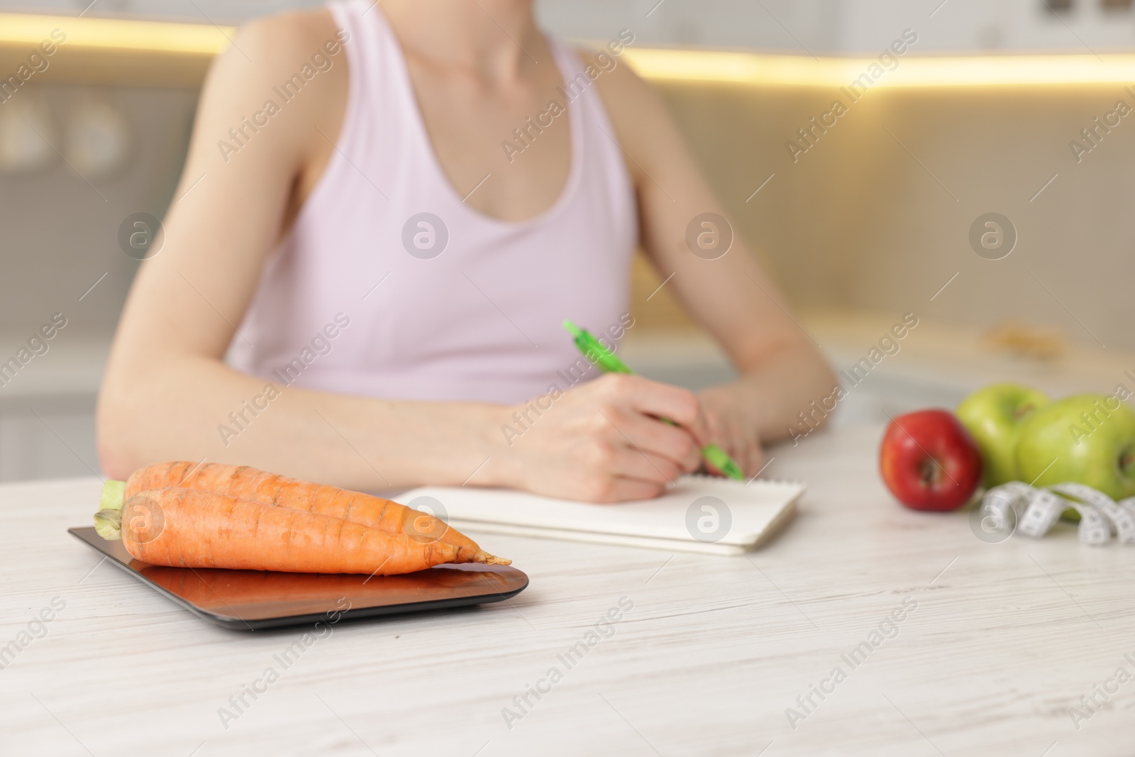 Woman developing diet plan at white wooden table indoors, focus on kitchen scale and carrots Photo of Woman developing diet plan at white wooden table indoors, focus on kitchen scale and carrots