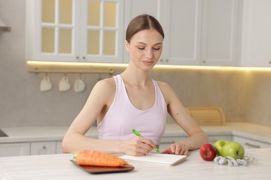 Photo of Woman developing diet plan at white wooden table indoors