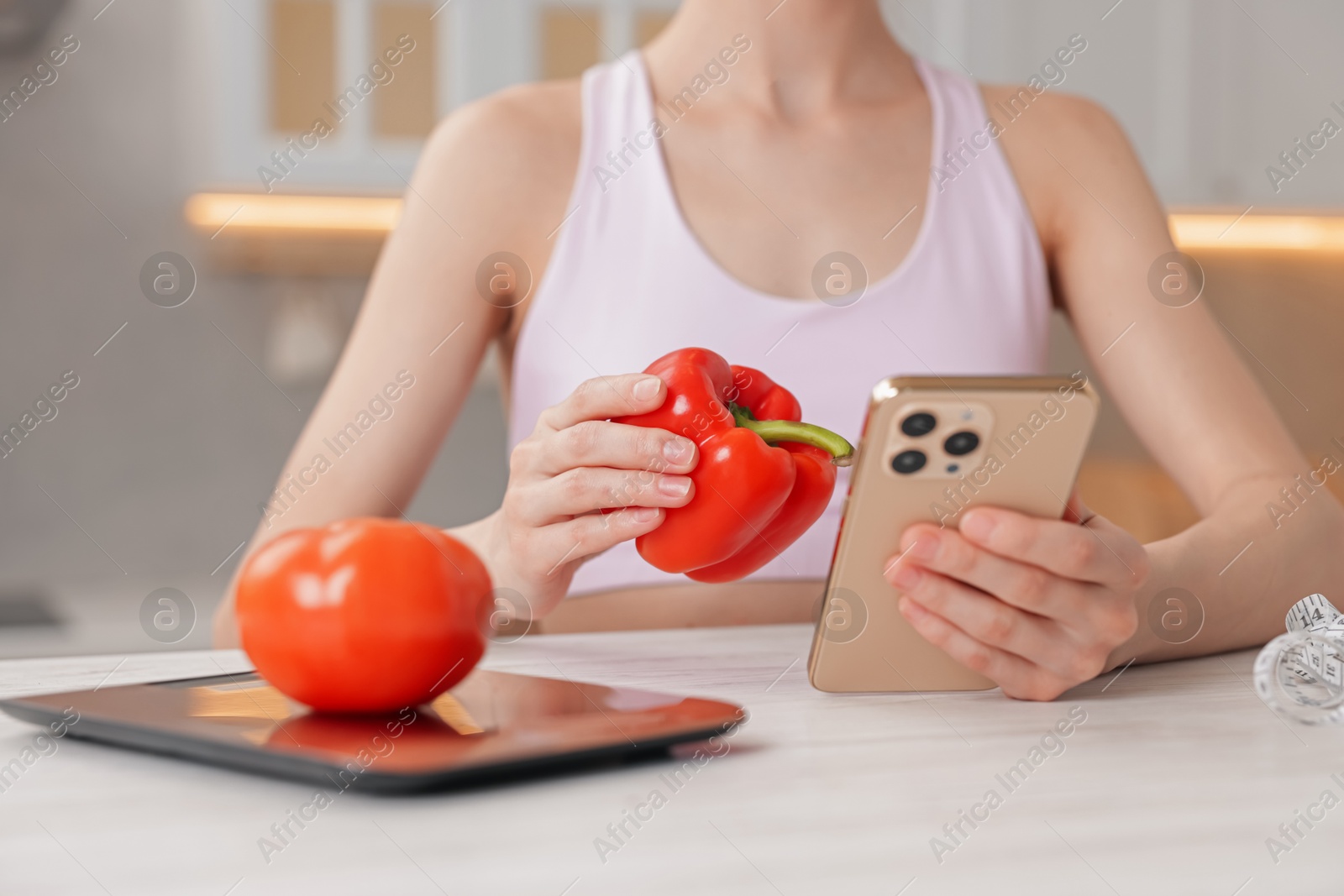 Woman with smartphone and bell pepper at white wooden table indoors, closeup Photo of Woman with smartphone and bell pepper at white wooden table indoors, closeup