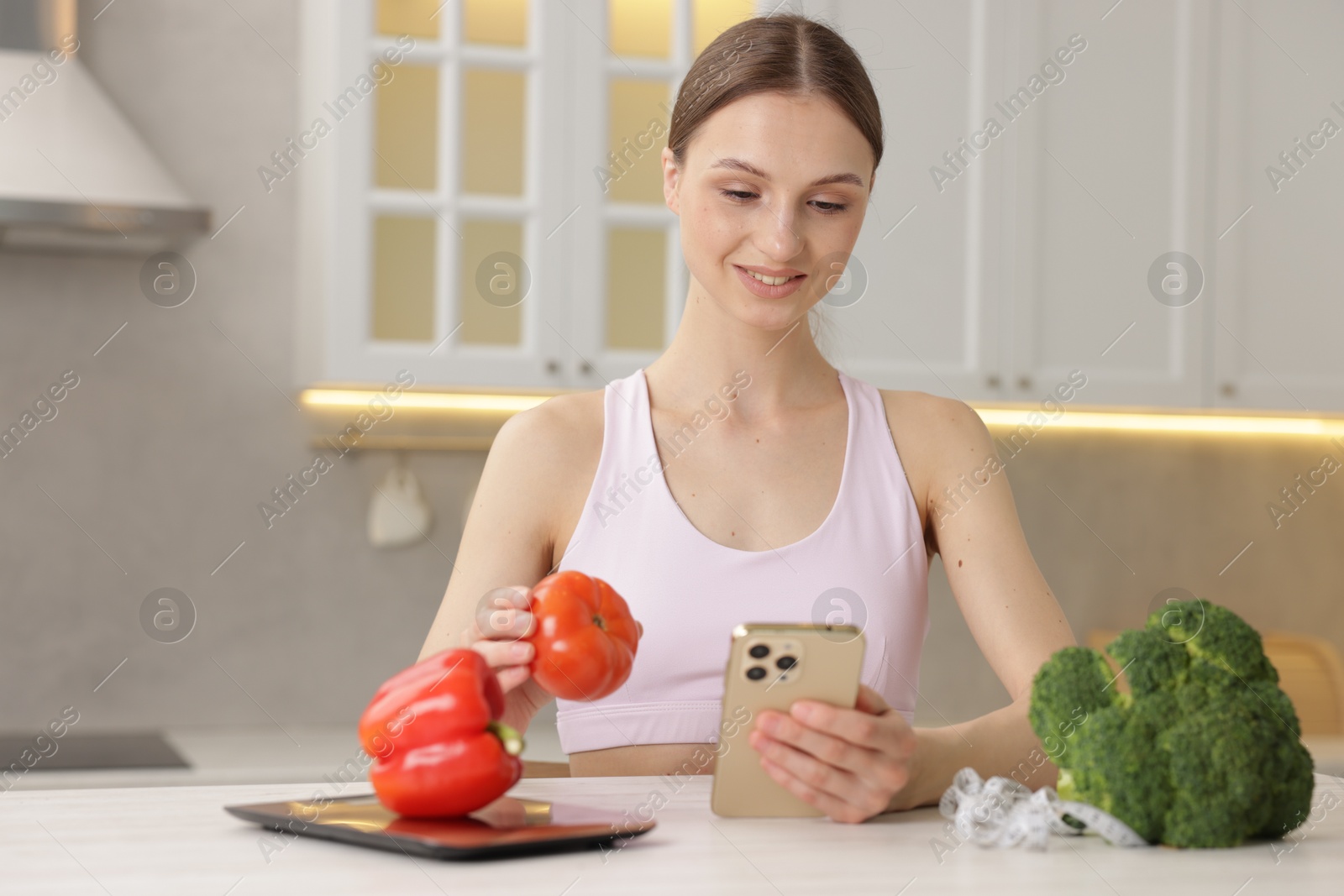 Woman with smartphone and tomato at white table indoors Photo of Woman with smartphone and tomato at white table indoors