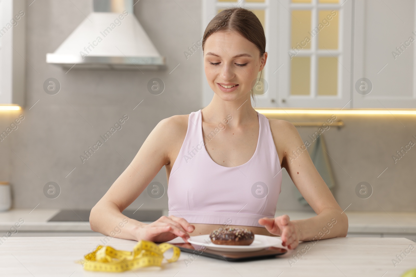 Woman weighting donut on kitchen scale at white table indoors Photo of Woman weighting donut on kitchen scale at white table indoors