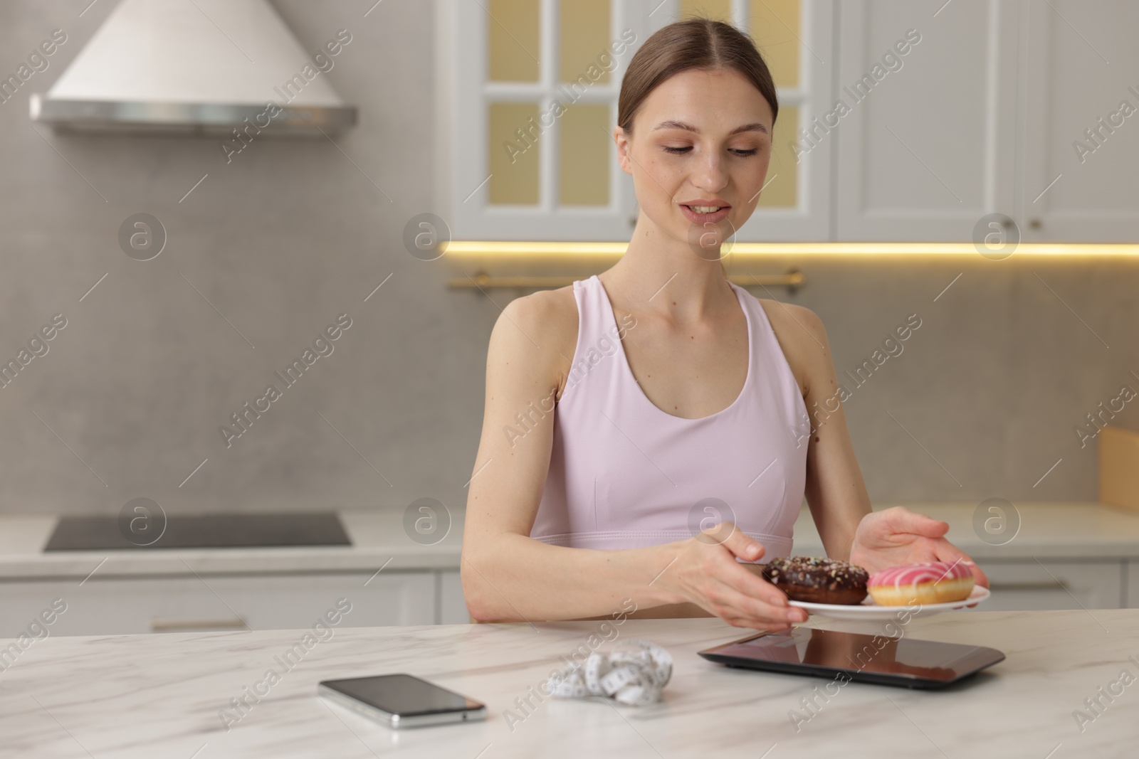 Woman weighing donuts on kitchen scale at white marble table indoors, space for text Photo of Woman weighing donuts on kitchen scale at white marble table indoors, space for text