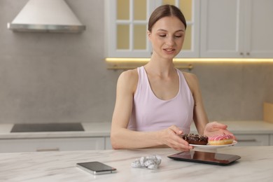 Photo of Woman weighing donuts on kitchen scale at white marble table indoors, space for text