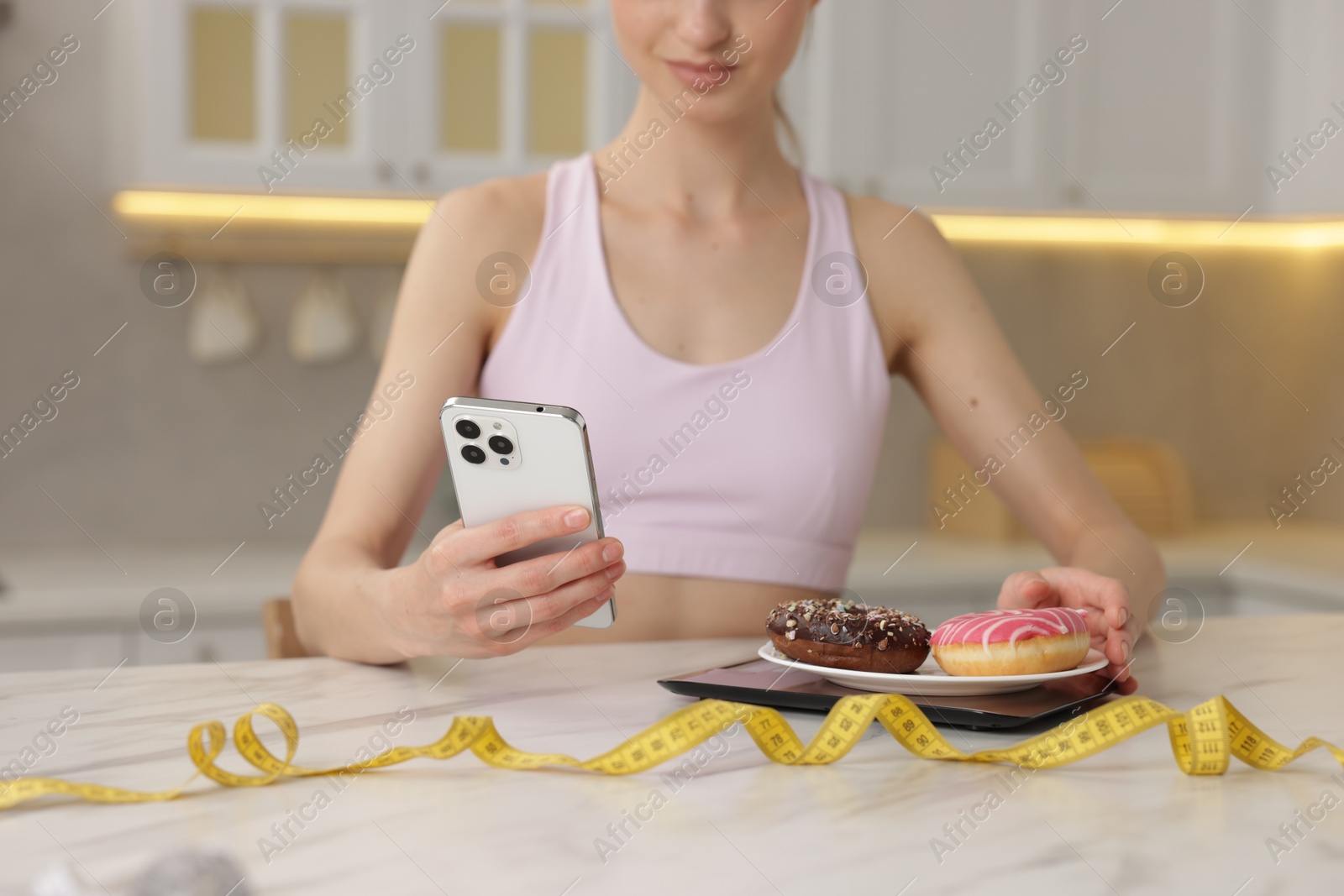 Woman with smartphone weighting donuts at white marble table indoors, closeup Photo of Woman with smartphone weighting donuts at white marble table indoors, closeup