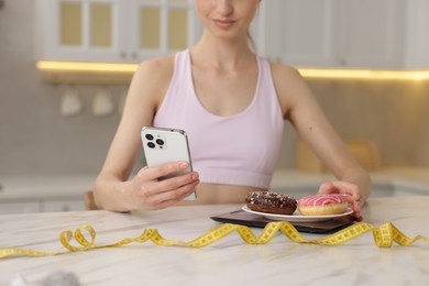 Photo of Woman with smartphone weighting donuts at white marble table indoors, closeup