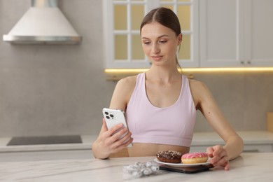 Photo of Woman with smartphone weighting donuts at white marble table indoors, space for text