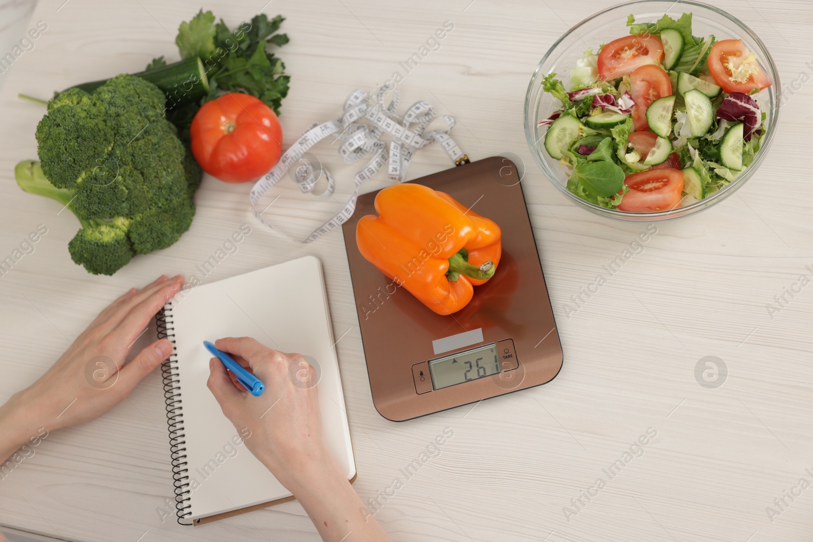 Photo of Woman developing diet plan at white wooden table with kitchen scale, healthy food and measuring tape, top view