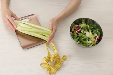 Photo of Woman weighting celery on kitchen scale at white wooden table, top view