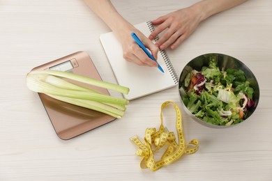 Photo of Woman developing diet plan at white wooden table with kitchen scale, healthy food and measuring tape, top view