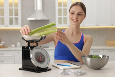 Photo of Woman weighting celery on kitchen scale at white table indoors