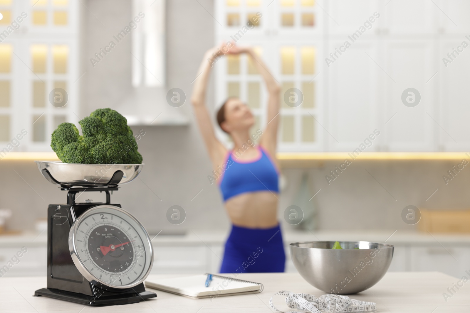 Slim woman posing indoors, focus on kitchen scale, broccoli, notebook, measuring tape and salad Photo of Slim woman posing indoors, focus on kitchen scale, broccoli, notebook, measuring tape and salad