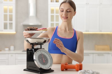 Photo of Woman weighting donuts on kitchen scale at white table indoors