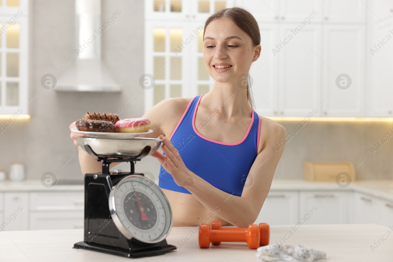 Woman weighting donuts on kitchen scale at white table indoors Photo of Woman weighting donuts on kitchen scale at white table indoors