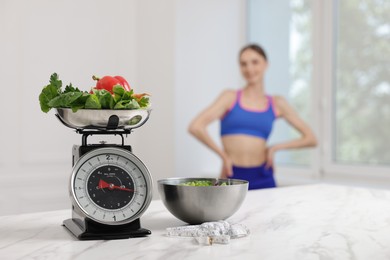 Photo of Slim woman posing indoors, focus on kitchen scale, vegetables, measuring tape and salad