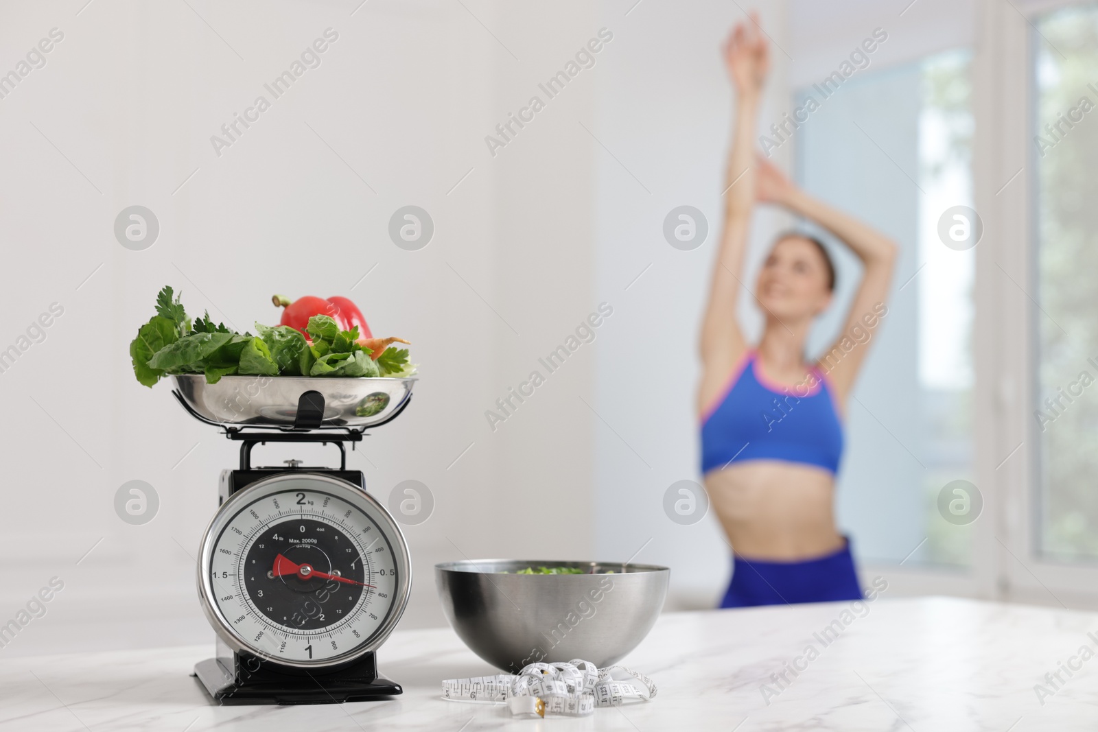 Slim woman posing indoors, focus on kitchen scale, vegetables, measuring tape and salad Photo of Slim woman posing indoors, focus on kitchen scale, vegetables, measuring tape and salad