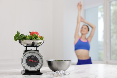Photo of Slim woman posing indoors, focus on kitchen scale, vegetables, measuring tape and salad