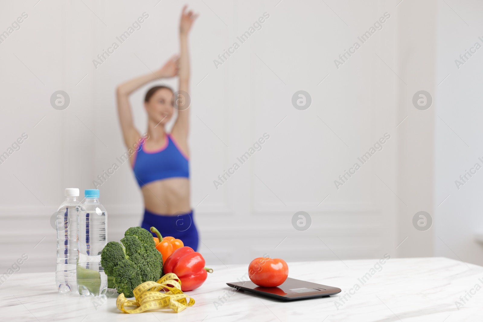 Slim woman posing indoors, focus on vegetables, measuring tape, water and kitchen scale Photo of Slim woman posing indoors, focus on vegetables, measuring tape, water and kitchen scale