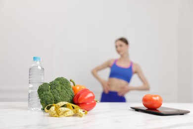Photo of Slim woman posing indoors, focus on vegetables, measuring tape, water and kitchen scale
