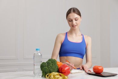 Photo of Woman developing diet plan at white marble table indoors, space for text