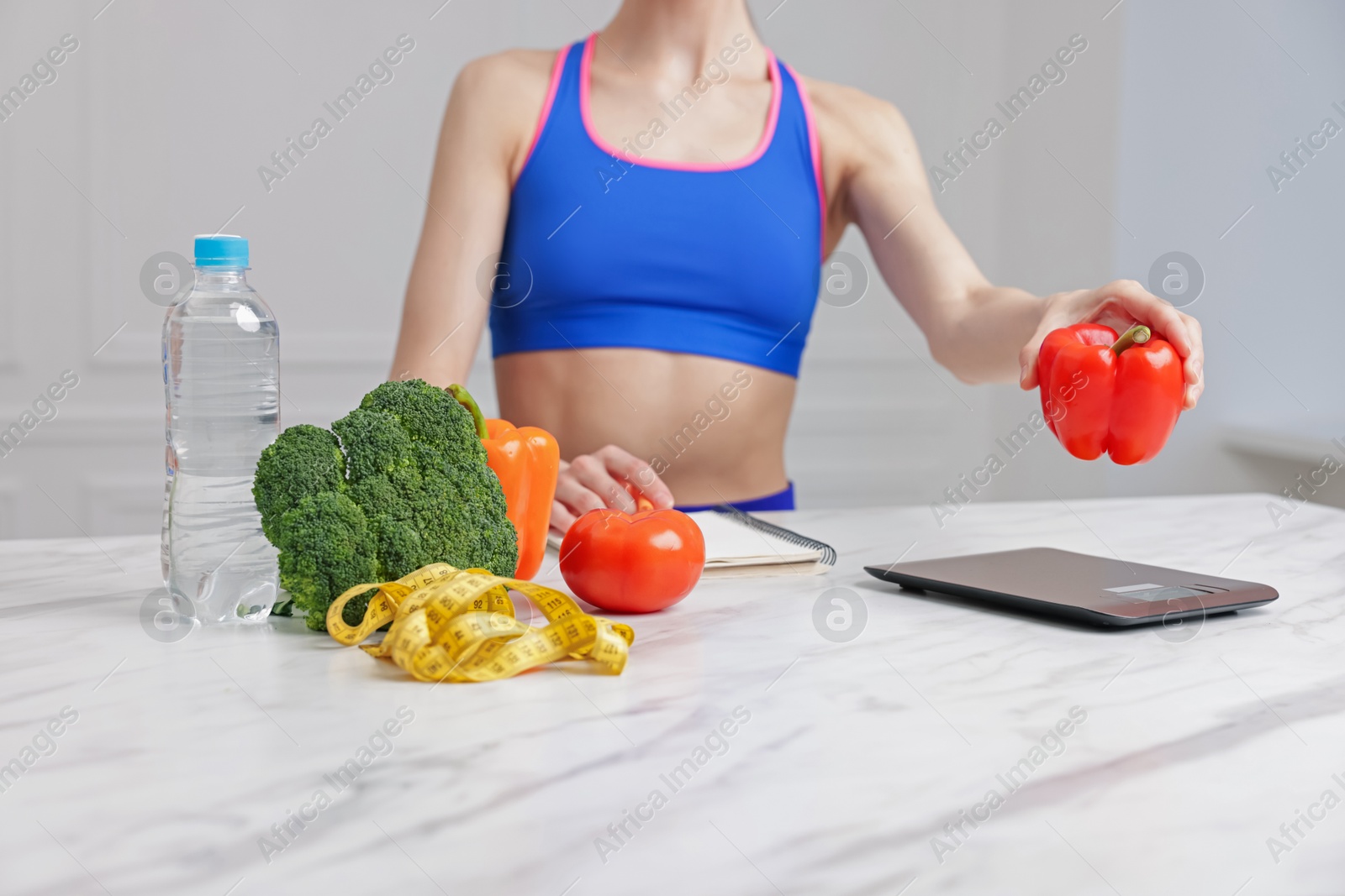Photo of Woman weighting bell pepper on kitchen scale at white marble table indoors, closeup