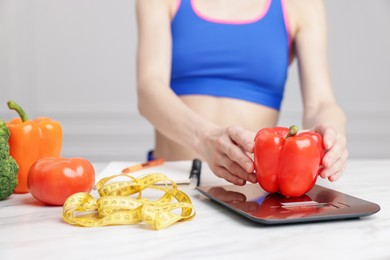 Photo of Woman weighting bell pepper on kitchen scale at white marble table indoors, closeup