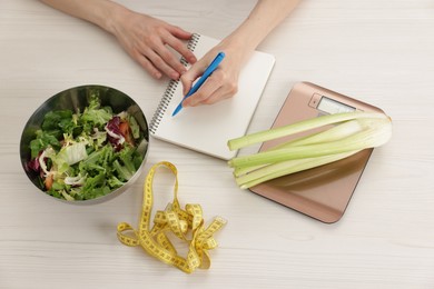 Photo of Woman developing diet plan at white wooden table with kitchen scale, measuring tape and healthy food, top view