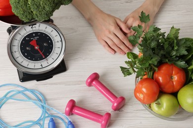 Photo of Woman at light wooden table with healthy food, kitchen scale, skipping rope and dumbbells, top view