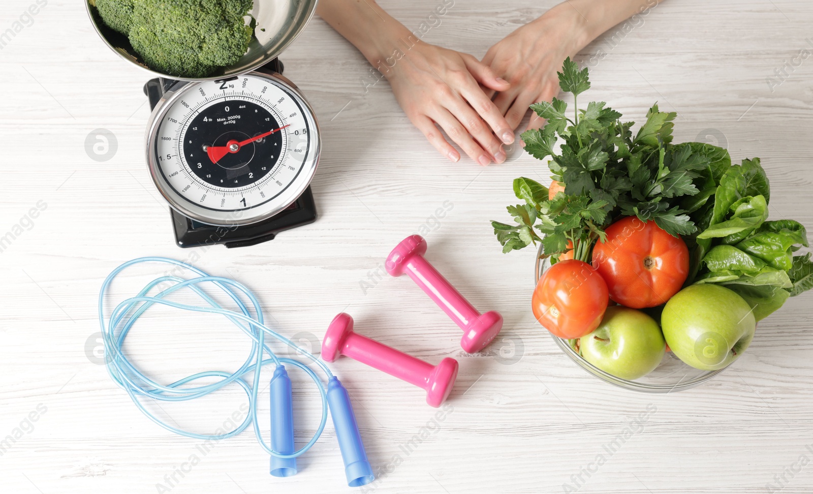 Woman at light wooden table with healthy food, kitchen scale, skipping rope and dumbbells, top view Photo of Woman at light wooden table with healthy food, kitchen scale, skipping rope and dumbbells, top view
