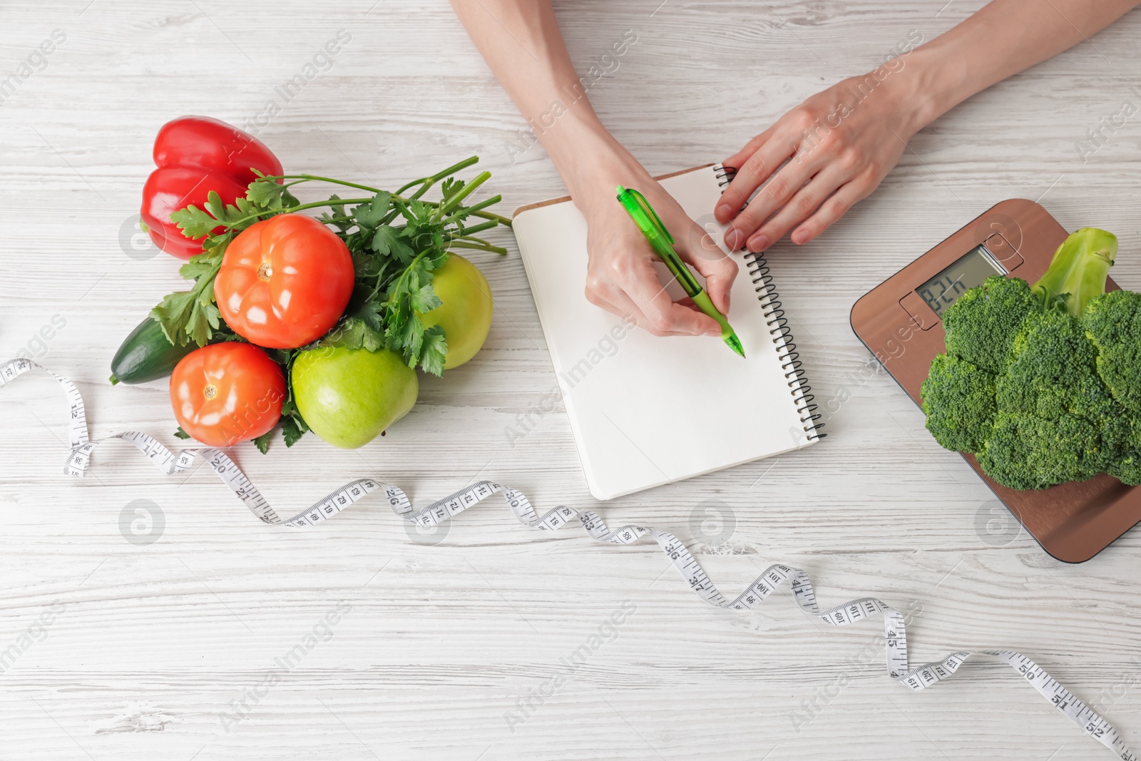 Woman developing diet plan at light wooden table with kitchen scale, measuring tape and healthy food, top view Photo of Woman developing diet plan at light wooden table with kitchen scale, measuring tape and healthy food, top view