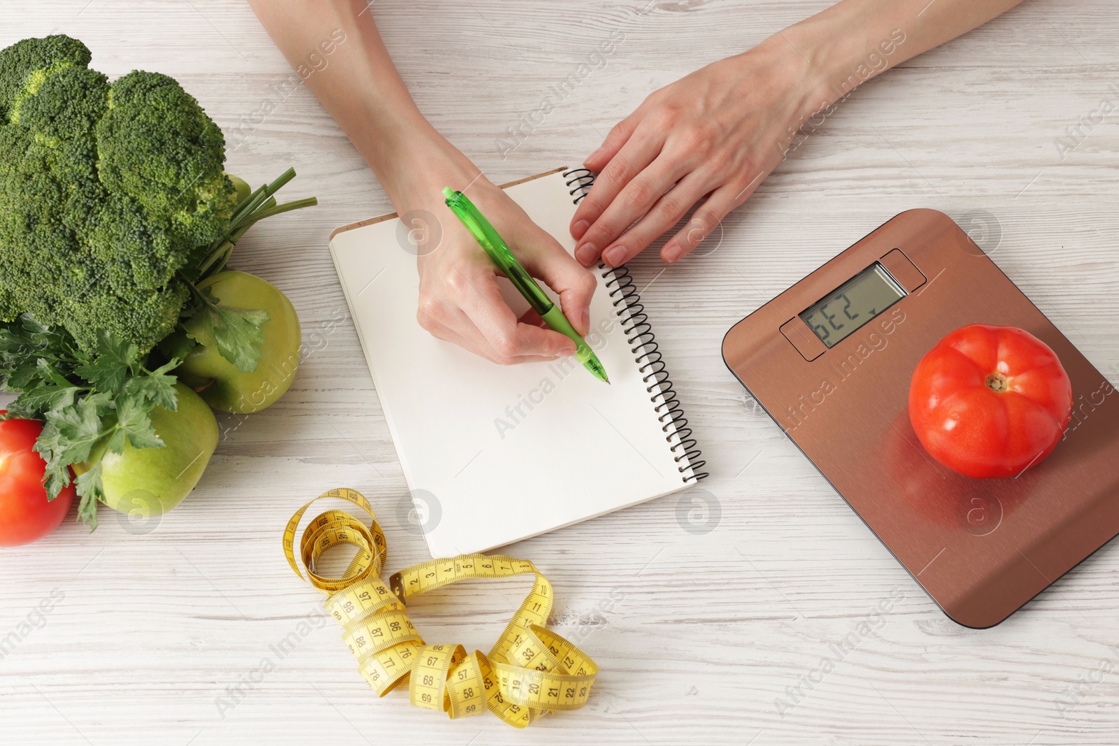 Woman developing diet plan at light wooden table with kitchen scale, measuring tape and healthy food, top view Photo of Woman developing diet plan at light wooden table with kitchen scale, measuring tape and healthy food, top view
